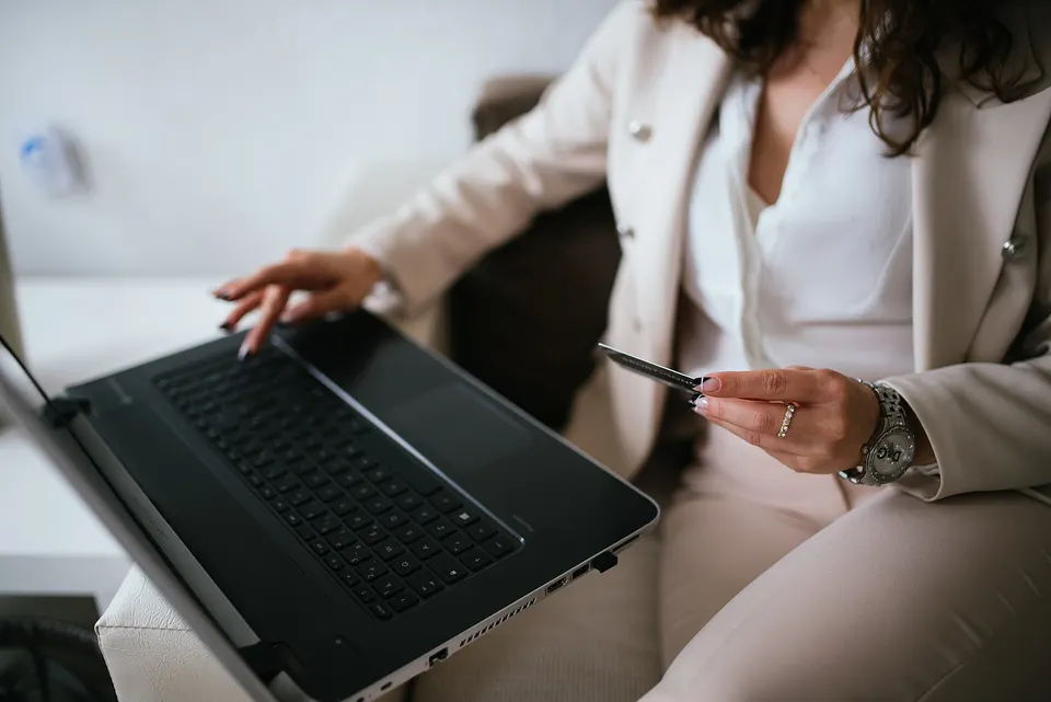 A person at a home desk holding a credit card while shopping online on a laptop